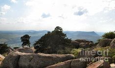 some rocks and trees on top of a hill with mountains in the distance behind them