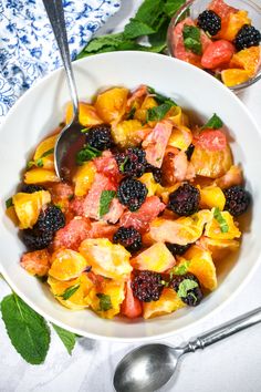 a white bowl filled with fruit salad next to two spoons on top of a table