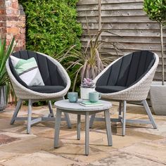 two chairs and a table sitting on a patio with plants in the backgroud