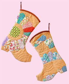 two quilted boots hanging from hooks on a pink background, one has a colorful patchwork design