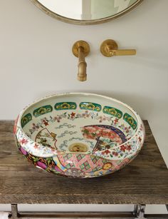 a bowl shaped sink sitting on top of a wooden table next to a wall mounted mirror