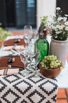 the table is set with wine glasses, bottles and succulents on it