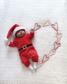 a baby wearing a santa hat laying on top of a white blanket with candy canes in the shape of a heart