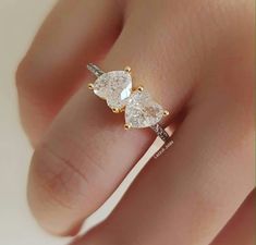 a woman's hand wearing a yellow gold ring with two pear shaped diamonds