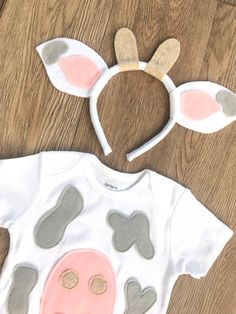 a white shirt with grey and pink ears on it sitting on top of a wooden floor