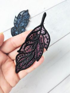 a hand holding two small black and pink lace leaves