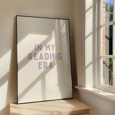 a framed poster with the words in my reading era on it next to a window