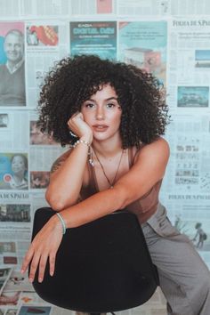 a woman sitting on top of a chair in front of a wall covered with newspapers