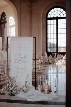 a white sign sitting on top of a table next to candles and vases filled with flowers