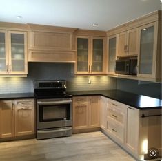 an empty kitchen with wooden cabinets and black counter tops on the island, along with stainless steel appliances