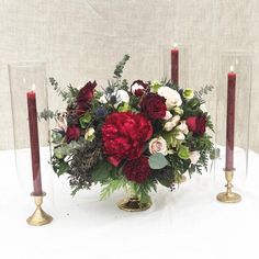 red and white flowers in a vase with candles on a round tablecloth covered table