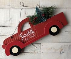 a red truck ornament hanging on a white wooden wall with christmas tree in the back