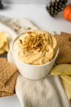 a white bowl filled with hummus next to crackers and apples