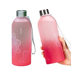 a hand holding a pink water bottle next to a red one with white designs on it