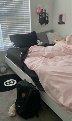 a bed with pink sheets and pillows in a bedroom next to a black duffle bag