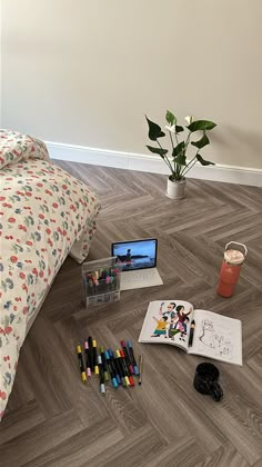 an open laptop computer sitting on top of a wooden floor next to markers and crayons