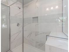 a bathroom with white marble walls and flooring, along with a walk in shower