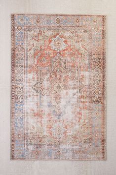 an old rug with faded colors and patterns on the ground in front of a white wall