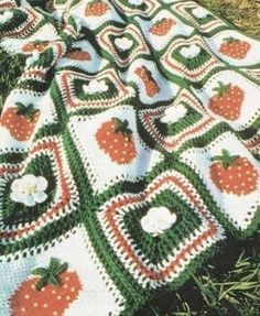 a crocheted blanket with apples and flowers on it is laying in the grass