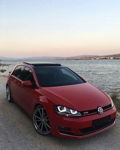 a red car parked on the side of a road next to some water and sand