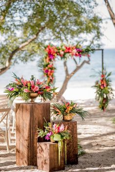 two wooden boxes with flowers on them are sitting in the sand near chairs and trees