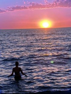 a woman standing in the ocean at sunset