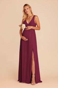 a pregnant woman in a purple gown with her legs crossed and holding a white flower