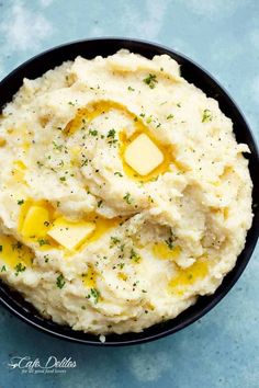 mashed potatoes with butter and parsley in a black bowl on a blue surface