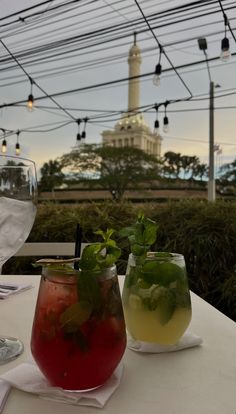 two glasses filled with drinks sitting on top of a white table next to each other