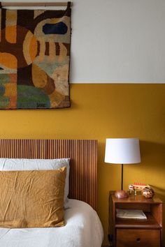 a bedroom with yellow walls and white bedding, two nightstands and a painting on the wall