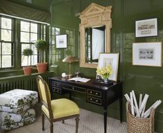 a desk with a chair and mirror in front of green painted walls, along with potted plants