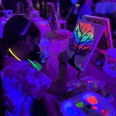 a woman is painting on an easel in the dark with neon lights around her