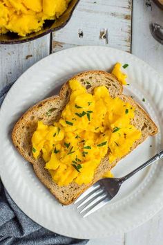 scrambled eggs on toast with butter and chives are served on a white plate next to a fork