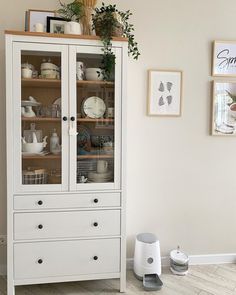 a white china cabinet with glass doors and drawers in a room that has pictures on the wall