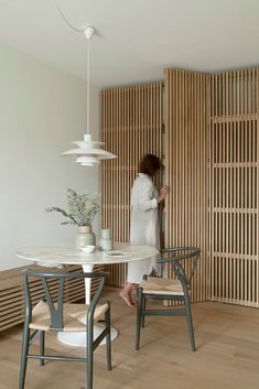 a woman standing in the corner of a room next to a table with chairs and vases on it