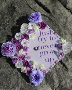 purple and white flowers are placed on top of a sign that says, just try to never grow up