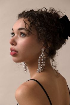 a woman with curly hair wearing earrings and a black bow on top of her head