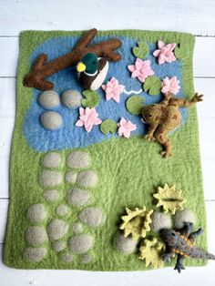 an animal rug with various felt animals and flowers on it, including a frog in the pond