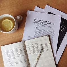 a cup of coffee and some papers on a table with a pen, lemon slice, and notebook