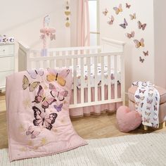 a baby crib with pink bedding and butterflies on the wall next to it