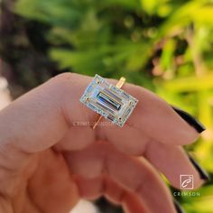 a person holding an engagement ring in their hand, with the diamond set on it's side