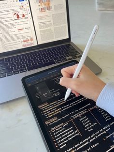 a person is writing on an ipad next to a laptop with a computer screen open