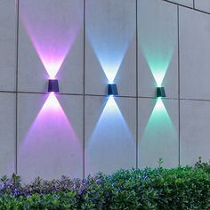 three different colored lights on the side of a building next to bushes and shrubbery