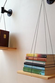 two books are suspended from the ceiling by hanging strings on wooden shelves with bookends