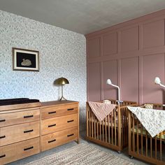 two baby cribs in a room with pink wallpaper and wooden dressers