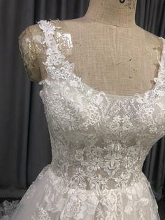 the back of a wedding dress with white lace and flowers on it, sitting on a mannequin