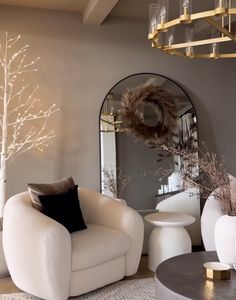 a living room filled with white furniture and a mirror on the wall next to a tree