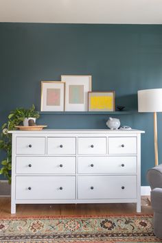 a white dresser sitting in a living room next to a lamp and pictures on the wall