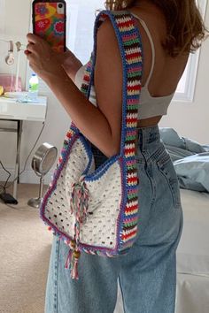 a woman holding a cell phone and wearing a crocheted bag with tassels