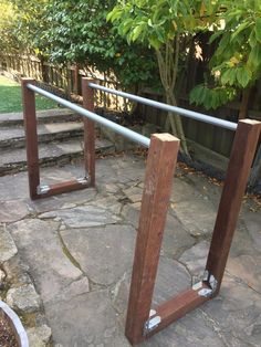 a metal rail sitting on top of a stone floor next to a tree and bushes